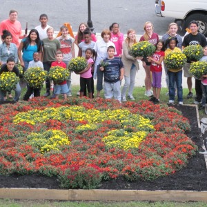A group of students holds flowers behind a planting of flowers